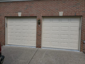 Two beige residential garage doors on a brick house, installed by Midland Glass and Garage Doors in Frederick, MD