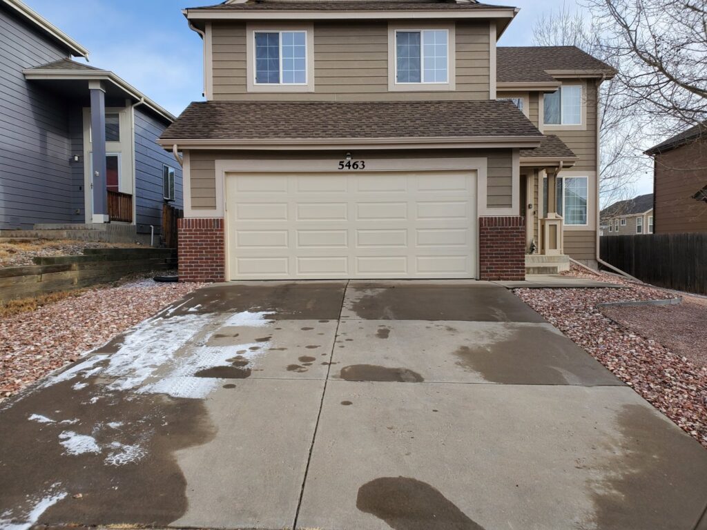 An exterior view of a beige sectional garage door on a house, serviced by Black Forest Door Repair in Colorado Springs, CO.