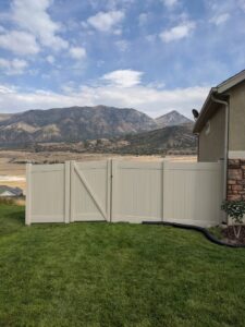 A beige vinyl privacy fence with a gate installed in a backyard with mountains in the background by All American Vinyl in Provo, UT.