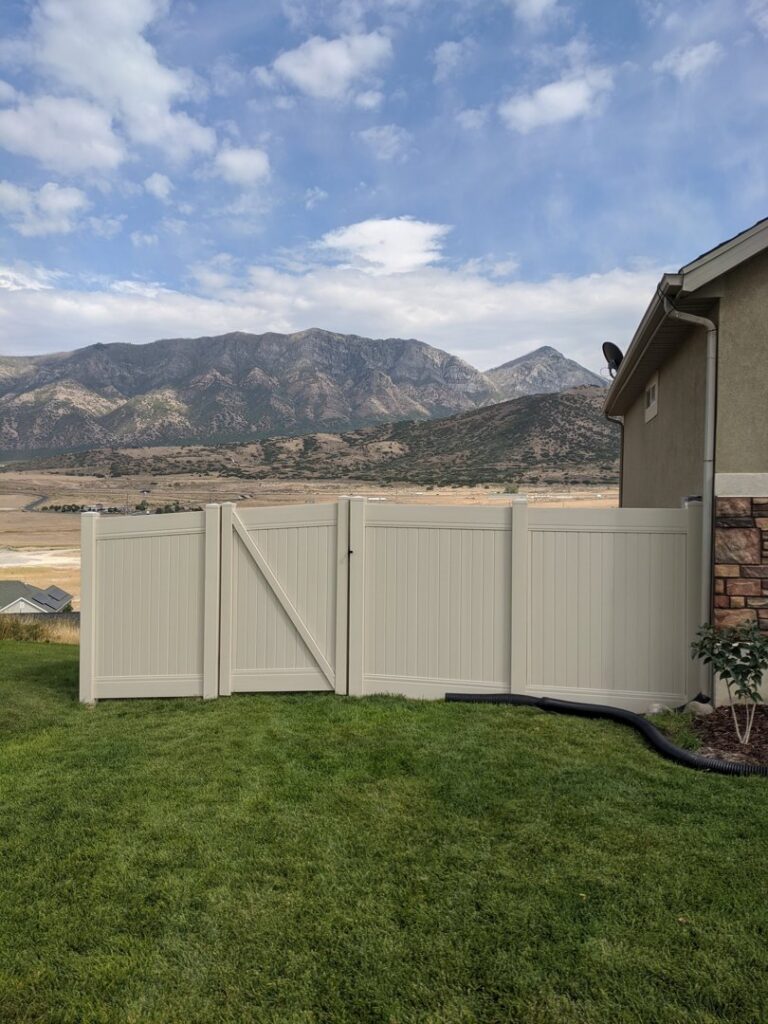 A beige vinyl privacy fence with a gate installed in a backyard with mountains in the background by All American Vinyl in Provo, UT.