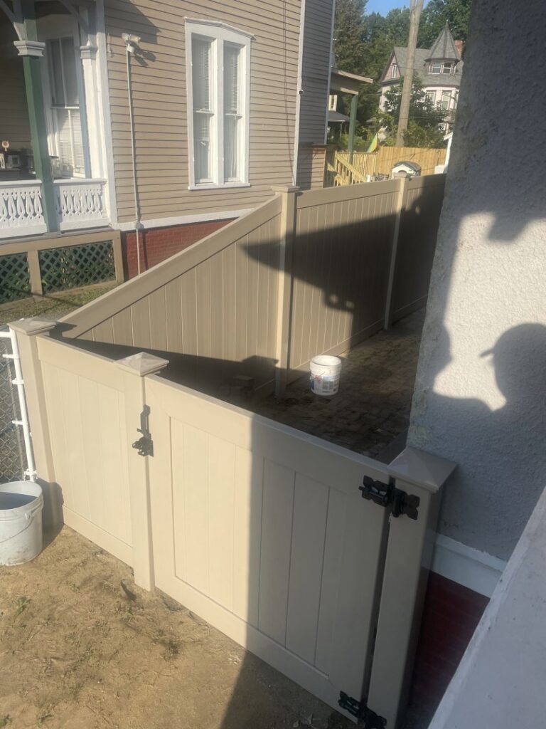 A beige vinyl privacy fence with a gate installed in a narrow space by Texeira Fencing & Concrete in Springfield, MA.