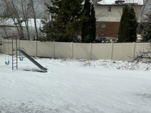 A beige vinyl privacy fence installed in a snowy residential backyard by All American Vinyl in Provo, UT.