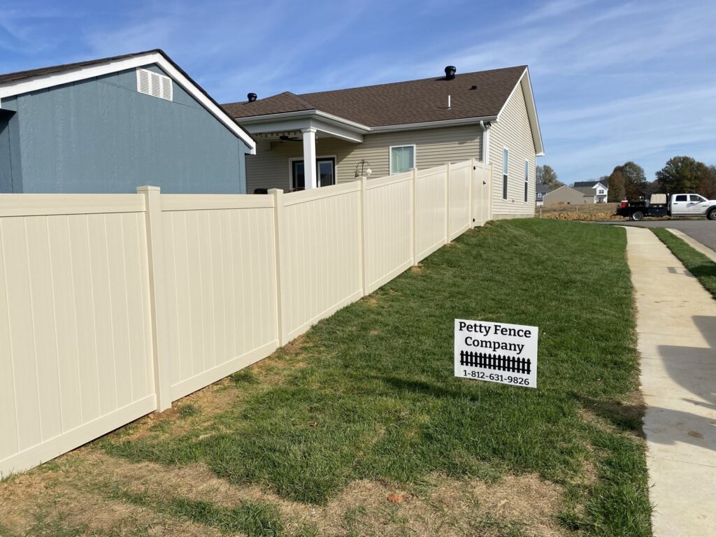 A newly installed beige vinyl privacy fence with a Petty Fence Company LLC sign in Evansville, IN.