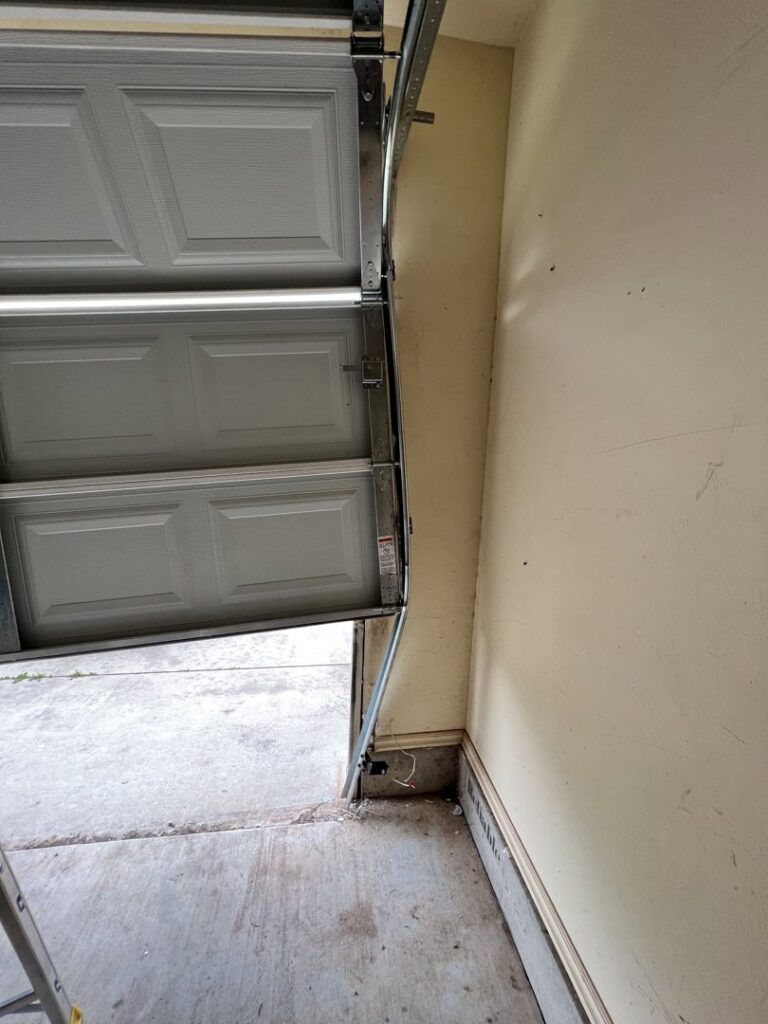 A bent garage door that is off its tracks, requiring repair services from Rhino Garage Doors LLC OKC in Edmond, OK.