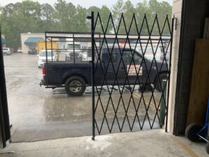 Black accordion-style security gate installed in a commercial doorway by Ability Burglar Bars in Jacksonville, FL.