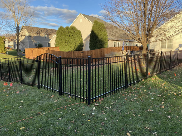 A newly installed black ornamental aluminum fence with an arched gate in a backyard by Safe Yard Fence - Waukesha County in Waukesha, WI.