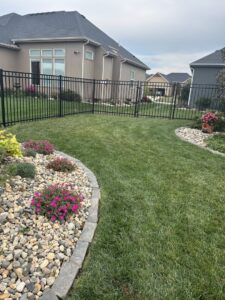 A black aluminum fence installed around a backyard with decorative landscaping by Royal Fence & Design LLC in Olathe, KS.
