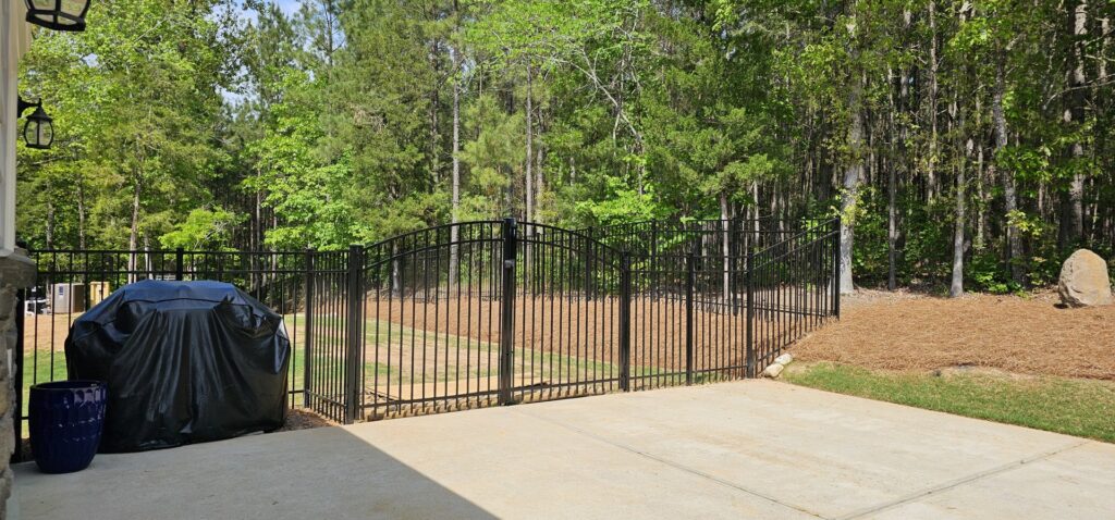 A black aluminum double gate installed at the edge of a patio leading to a backyard by Endurance Fence Solutions, LLC in Holly Springs, NC