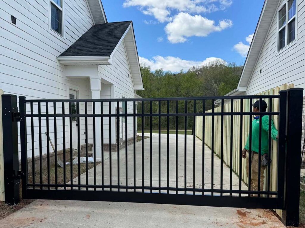 A large black aluminum driveway gate being installed between two homes by a RUCO Fence contractor in Huntsville, AL.