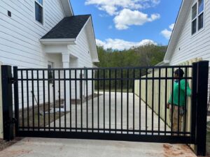 A large black aluminum driveway gate being installed between two homes by a RUCO Fence contractor in Huntsville, AL.