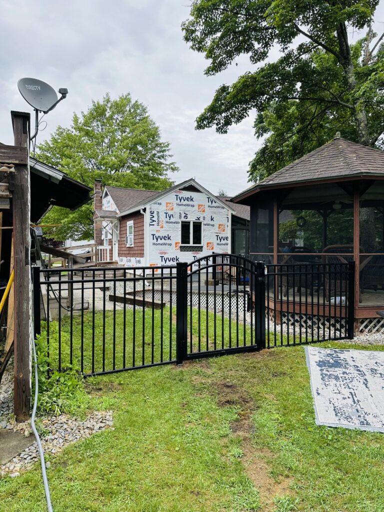 A black aluminum fence with a gate installed next to a house under construction by Ultra Fence LLC in Brookline, NH.