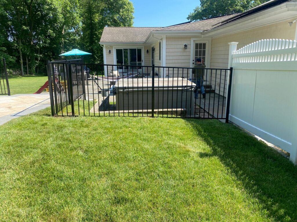 A sleek black aluminum fence enclosing a hot tub area, adjacent to a white vinyl fence, installed by AVA Fence & Railing LLC in Stamford, CT.