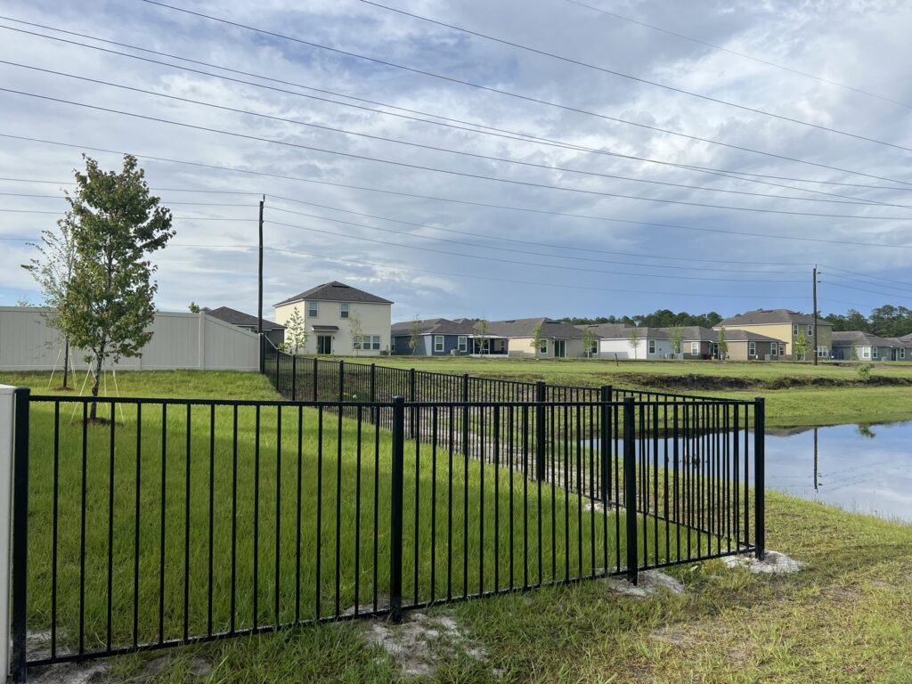 A black aluminum fence installed along a residential pond, offering safety and aesthetics by Fence Nation LLC in Jacksonville, FL.