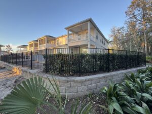 A black aluminum fence installed atop a stone retaining wall by Fence Nation LLC in Jacksonville, FL.