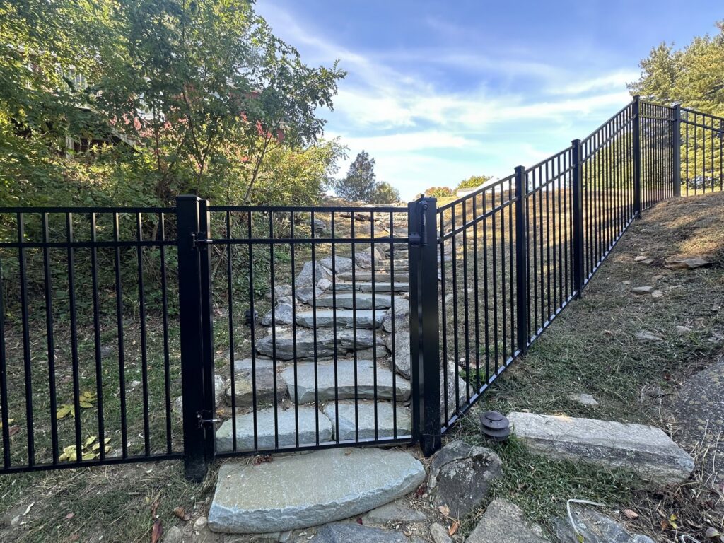 A black aluminum fence with a gate installed on a sloped, rocky terrain with stone steps by Quality Fence Inc. in Peekskill, NY