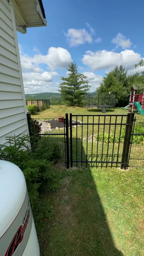 A black aluminum fence with a gate installed on a hillside overlooking a valley by Quality Fence Inc. in Peekskill, NY