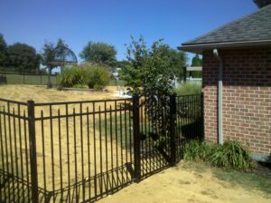 A black aluminum fence with a gate installed next to a brick house by Snyders Custom Fencing in York, PA.