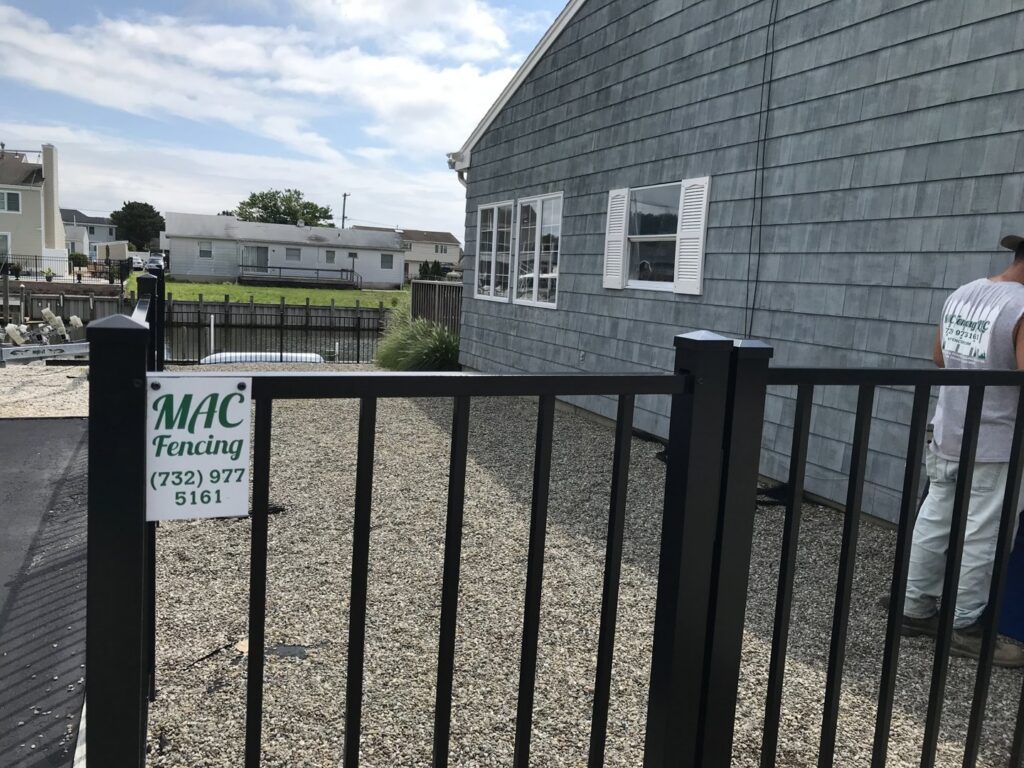 A black aluminum fence with a MAC Fencing LLC sign installed next to a house and waterway in Toms River, NJ