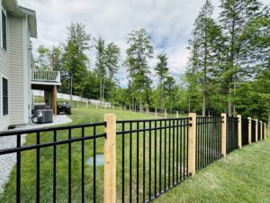 A modern black aluminum fence with sturdy wooden posts, installed on a grassy slope by Ultra Fence LLC in Brookline, NH.