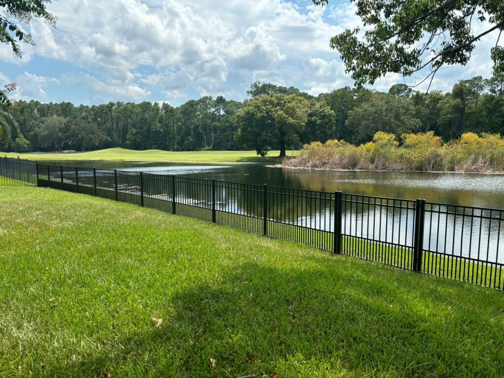 A sleek black aluminum fence installed along a lakefront property, offering safety and clear views by Exacta FENCE LLC in Jacksonville, FL.