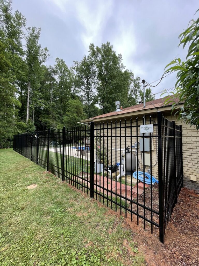 A black aluminum fence installed around a pool equipment area next to a house by TC Fencing LLC in Tuscaloosa, AL.