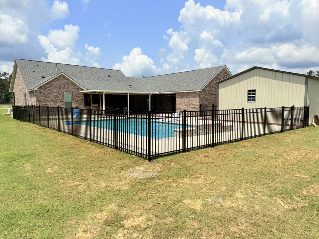 A black aluminum fence securely enclosing a swimming pool in a residential backyard, installed by Capitol Fencing in Baton Rouge, LA.