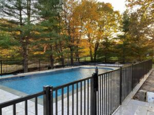 A black aluminum fence securing a swimming pool area with a sunset backdrop by Flanagan Fencing in Brookfield, CT.