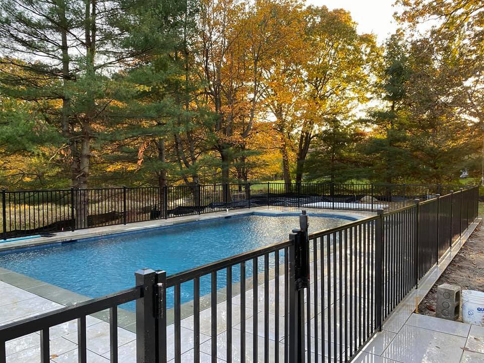 A black aluminum fence securing a swimming pool area with a sunset backdrop by Flanagan Fencing in Brookfield, CT.