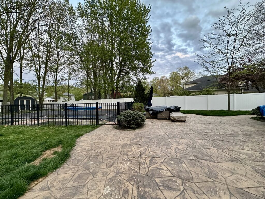 A backyard featuring a black aluminum pool fence and a white vinyl privacy fence by Budget Fence of Ohio in Cleveland, OH.