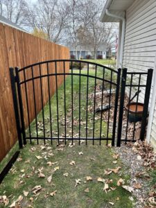 A black ornamental aluminum gate installed next to a wooden privacy fence in a side yard by Safe Yard Fence - Waukesha County in Waukesha, WI.
