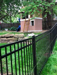 A black aluminum fence with an open gate around a basement window well by Royal Fence & Design LLC in Olathe, KS.