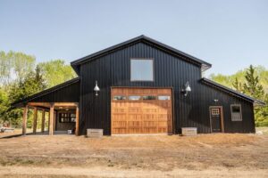 A large black barn-style building featuring a beautiful wooden garage door installed by Monroe Overhead Doors in Monroe, LA.
