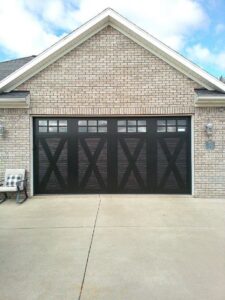 A stylish black carriage-style garage door with decorative X-patterns and windows, installed by JT's Overhead Doors in Gilbert, AZ.