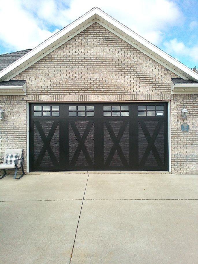 A stylish black carriage-style garage door with decorative X-patterns and windows, installed by JT's Overhead Doors in Gilbert, AZ.