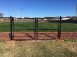 A black chain link fence with a double gate enclosing a baseball field by Precision Fence in Meridian, MS.