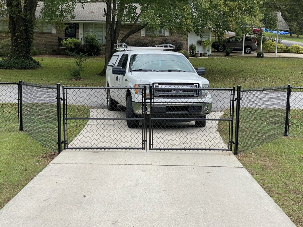 A newly installed black chain-link fence with a double gate for a residential driveway by Premier Fence of Birmingham, LLC in Warrior, AL.