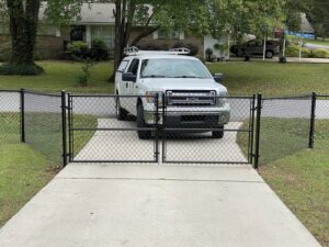 A newly installed black chain-link fence with a double gate for a residential driveway by Premier Fence of Birmingham, LLC in Warrior, AL.