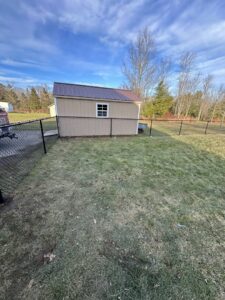A newly installed black chain-link fence surrounding a backyard shed by Vision One Construction in Schenectady, NY