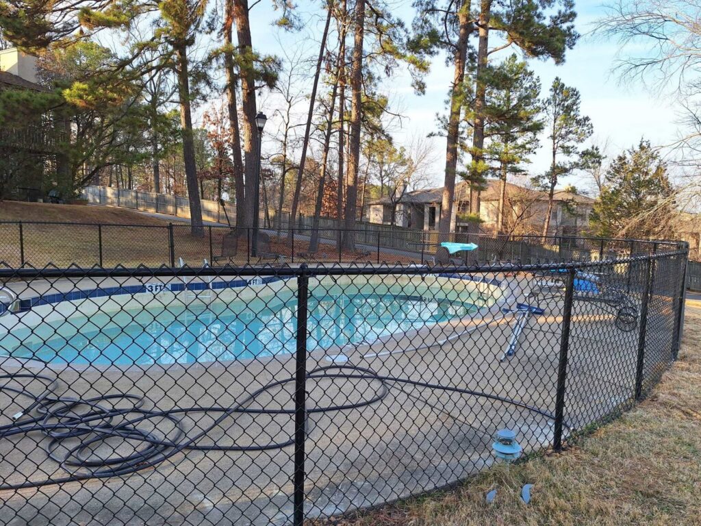 A black chain-link fence enclosing a swimming pool area by Fences & Landscape Inc in Little Rock, AR.