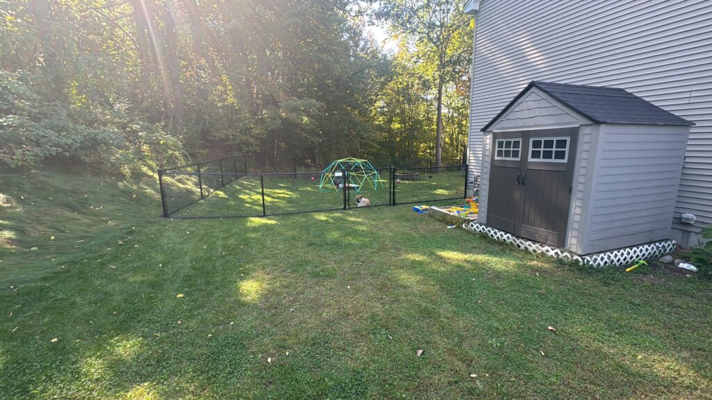 A black chain-link fence securing a backyard with a shed and play area by Precision Fence NH in Hooksett, NH.