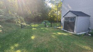 A black chain-link fence securing a backyard with a shed and play area by Precision Fence NH in Hooksett, NH.