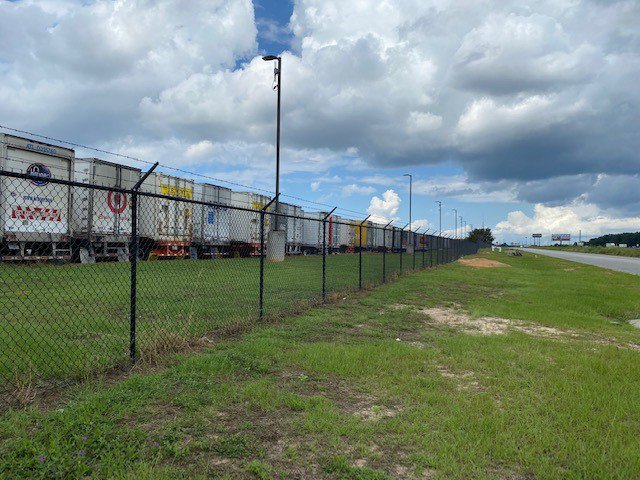 A long black chain link fence with barbed wire securing a commercial property alongside a road, by National Fence Services, LLC in Macon, GA.