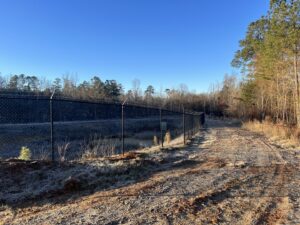 A black chain-link fence with barbed wire installed along a dirt path by East Georgia Fence in Evans, GA.
