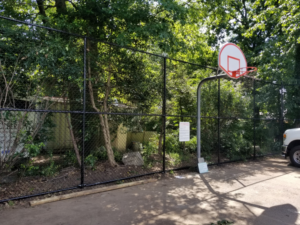 A durable black chain-link fence installed around a recreational area with a basketball hoop by Fox Fence Enterprises Inc in Clifton, NJ.