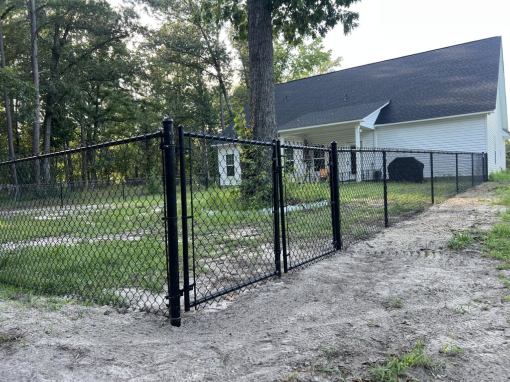 A newly installed black chain link fence with a double gate in a residential backyard by Fayetteville Fence Pros in Fayetteville, NC.