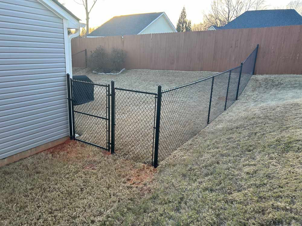 A newly installed black chain-link fence with a gate in a residential backyard by FenceMax in Spartanburg, SC