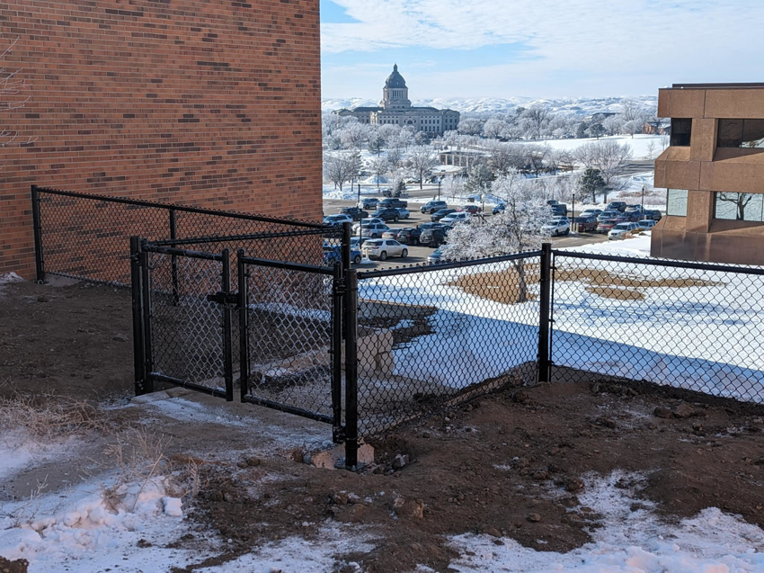 Black chain-link fence with a gate installed on a snowy hillside by Solid Fence Co. in Sioux Falls, SD.