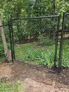 A newly installed black chain-link fence with an open gate in a natural setting by Superior Fence & Rail of Arkansas in Springdale, AR.