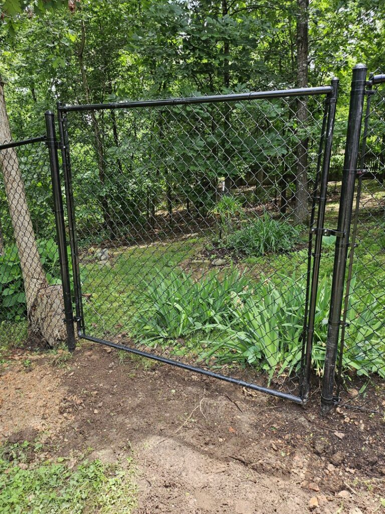 A newly installed black chain-link fence with an open gate in a natural setting by Superior Fence & Rail of Arkansas in Springdale, AR.