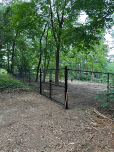 Black chain-link fence with a double gate installed in a natural, wooded backyard by New England landscaping and fence inc in Lynn, MA.